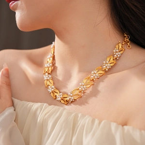 Detail of vintage gold necklace featuring pearl inlaid leaf pendant worn on model
