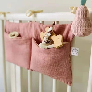 Detail of pink double-pocket cotton nursery organizer hanging on a white crib railing