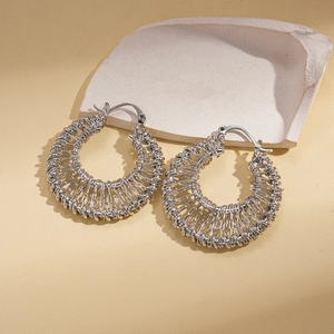 Detailed close-up of silver woven hollow hoop earrings on a textured stone surface