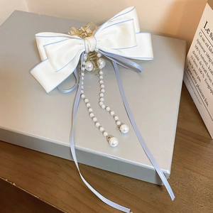 Detailed view of ivory satin bow hair claw with pearl tassels and blue trim details