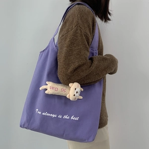 Purple canvas shoulder bag with cat plush charm shown in a lifestyle model shot