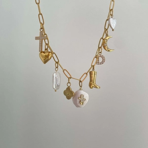 Detailed shot of gold plated necklace with various charms like pearl and heart pendants