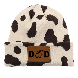 Detail of knitted cow print beanie featuring a brown leather patch with DAD text