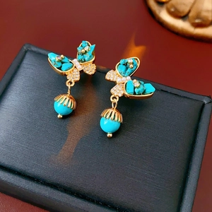 Vue détaillée de boucles d'oreilles papillon dorées avec incrustation de turquoise et perle