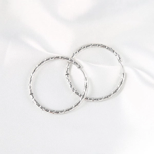 Minimalist silver hammered round hoop earrings set on white silk background texture