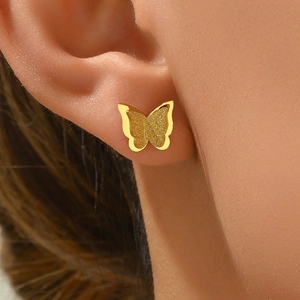 Elegantes pendientes de mariposa dorados con acabado mate y pulido puestos en la oreja