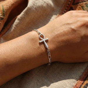 Detail of silver Ankh cross bracelet on Figaro chain worn on wrist with vintage texture
