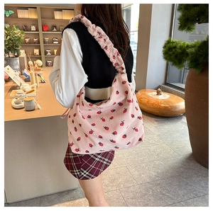 Detail view of pink corduroy shoulder bag with strawberry embroidery and elastic strap