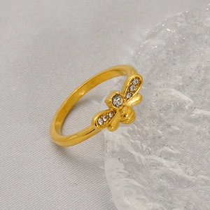 Gold tone titanium steel bee ring with white crystal inlay on a gray fabric background