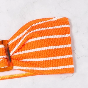 Close-up of orange striped smocked bikini fabric with an amber resin buckle detail