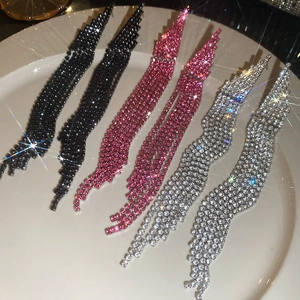 Close-up of tassel earrings with rhinestones in black, pink, and silver on a plate