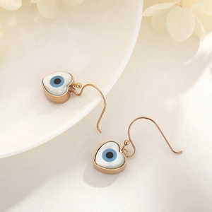 Detail of rose gold heart earrings featuring blue evil eye charms on ceramic background