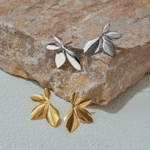 Detailed view of gold and silver leaf-shaped stainless steel earrings on natural rock