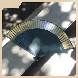 Vintage green gradient folding fan with hollow pattern on a stone surface