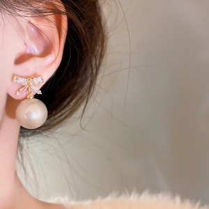 Close-up of elegant bow-shaped gold earrings with sparkling zircon and round white pearl