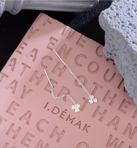 Detailed macro view of silver clover long tassel drop earrings on a pink pedestal