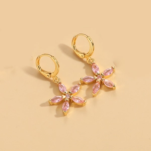 Detail of gold hoop earrings with pink flower-shaped gemstone pendants on beige surface