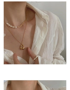 Close-up of layered gold chain pearl necklace and organic pendant on a white shirt