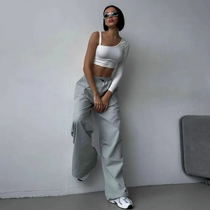 Dettaglio del completo con crop top bianco monospalla e pantaloni sportivi grigi larghi