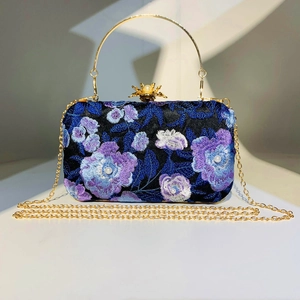 Detail of floral embroidery and pearl accents on a black evening clutch with gold chain