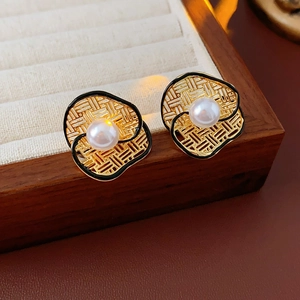 Detail of flower-shaped gold-plated stud earring with woven texture and a central white pearl