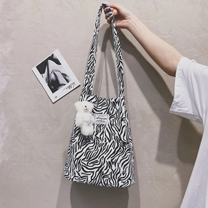 Detail of zebra print canvas tote bag featuring a plush bear charm and brand label