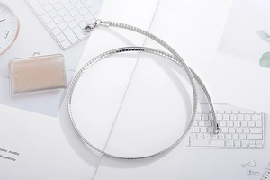 Detail of silver snake chain necklace coiled in a circular layout on white background