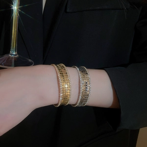 Detailed view of layered metallic bangle with scale texture and rhinestone edges