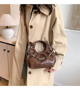 Close-up of dark brown pleated cloud bag with metallic bead chain on beige coat