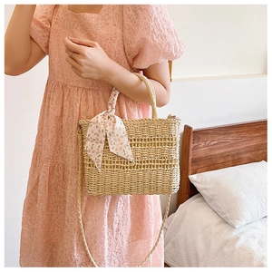 Detail view of woven straw handbag featuring a floral silk scarf and woven top handle