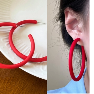 Detail view and model wearing large red matte hoop earrings on white embossed plate
