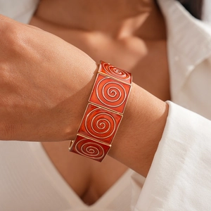 Detail of vintage orange enamel bracelet with golden spiral texture on model wrist