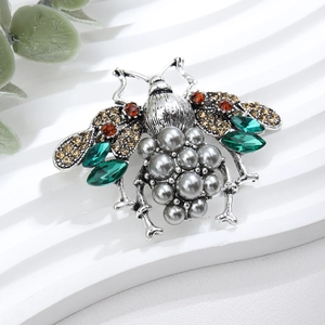 Macro detail of bee brooch featuring grey pearls and green marquise crystals
