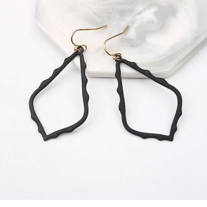 Matte black hollow teardrop leaf earrings with golden hooks on marble tray