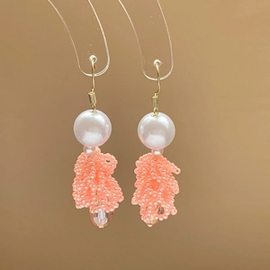 Détail de boucles d'oreilles à pompons en perles corail avec perles blanches et crochets d'or