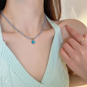 Close-up of a blue heart-shaped opal pendant on a beaded necklace and a gold crown ring