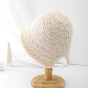 Detailed close-up of cream knit bucket hat texture on a minimalist wooden stand