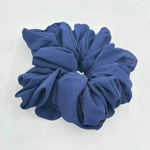 Detail view of a large navy blue chiffon hair scrunchie with soft ruffled texture on white