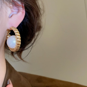Macro shot of gold-plated textured hoop earrings with a large white pearl inlay