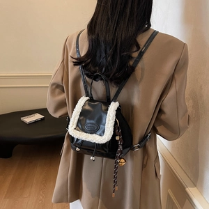 Black leather and white plush backpack with bell pendant worn by a model in interior