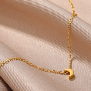 Detail of a gold crescent moon pendant on a fine cross chain over champagne silk