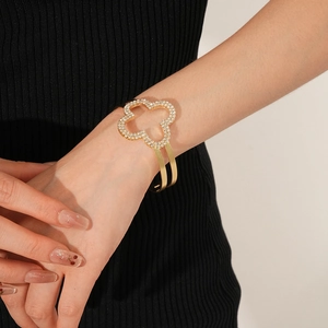 Dettaglio di un bracciale aperto dorato con un design a quadrifoglio impreziosito da strass