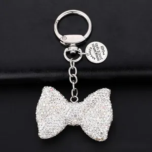 Detailed view of silver bowknot keychain with rhinestones and circular metal logo tag