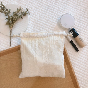 Detailed embroidery on white lace drawstring pouch with floral patterns and cotton rope