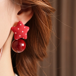 Close-up of red star fabric earring with white dots and glossy pearl worn by a model