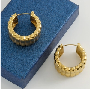 Detail of chunky gold U-shaped hoop earrings with vertical stripe texture on jewelry box