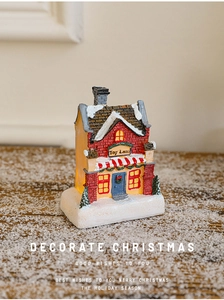 Close-up of a glowing Toy Land Christmas house with snow texture on a wooden surface