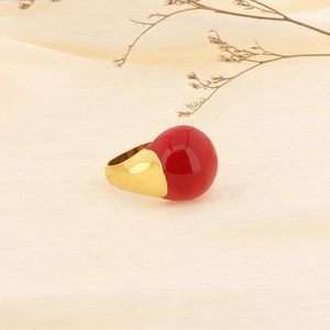 Detail of minimalist 18k gold ring with a large spherical red enamel stone on soft fabric