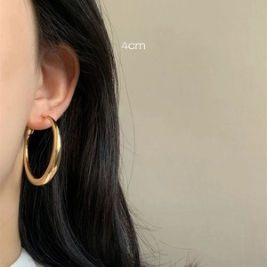 Close-up of 4cm thick gold hoop earring worn by a model against a neutral backdrop