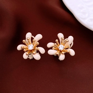 Dettaglio di orecchini a fiore bianco opaco con petali dorati su tessuto di seta